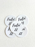 Five round white stickers with black text reading 'Feelin' 22' arranged on a textured off-white background.
