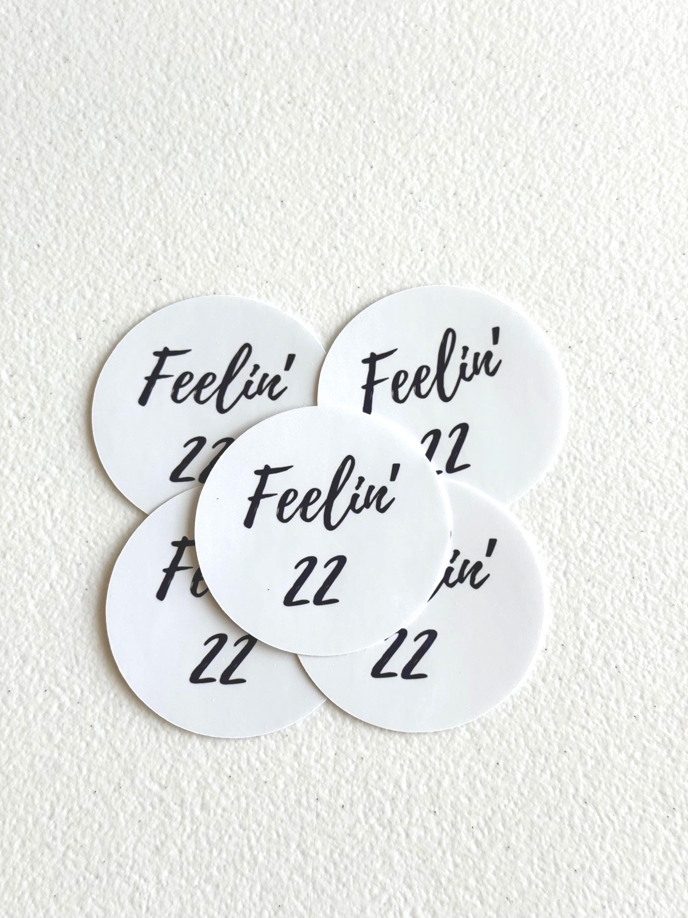 Five round white stickers with black text reading 'Feelin' 22' arranged on a textured off-white background.