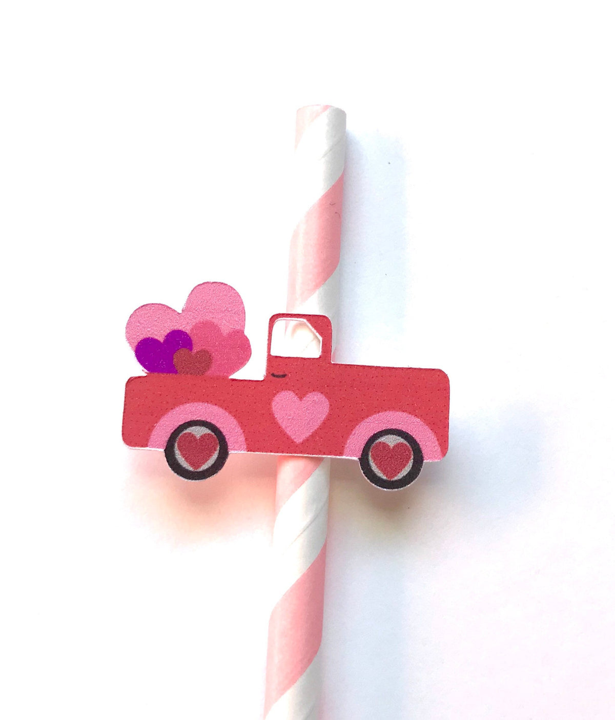 A pink and red paper cutout of a pickup truck with hearts on the side, attached to a pink and white striped paper straw against a white background.