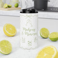 A white insulated can cooler sleeve with green champagne-themed illustrations and the text 'Majjong & Mimosas' stands on a white kitchen counter, surrounded by sliced lemons and limes.