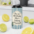 A slim can cooler sleeve with blue and white vertical stripes and a central cream label reading 'Buoy Oh Buoy, She's Getting Married' in black script and serif text, styled on a kitchen counter with lemons and limes.