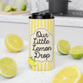 A yellow and white striped can cooler sleeve with the text 'Our Little Lemon Drop' stands on a white countertop, surrounded by fresh lemon slices and limes in a kitchen setting.