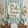 Nautical-themed 'Ahoy To The Future Mrs.' party backdrop setup with a blue and white striped tapestry, gold and silver balloons, floral arrangements, candles, and anchor decorations on a wooden table.