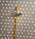 A Halloween-themed straw with a glittery black bat topper and a metallic gold tube, set against a gray patterned background with white and gold triangles.