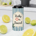 A tall insulated can cooler with a navy and white striped pattern and a cream label reading 'Baby on Board' with a small red-and-white life buoy icon. The cooler is shown on a kitchen counter surrounded by lemon halves and limes, with a stove and mug blurred in the background.