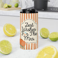 A slim can cooler sleeve with orange and white vertical stripes and the text 'Zest Wishes For The Mrs.' stands on a white countertop, surrounded by sliced lemons and limes, with a blurred kitchen background.