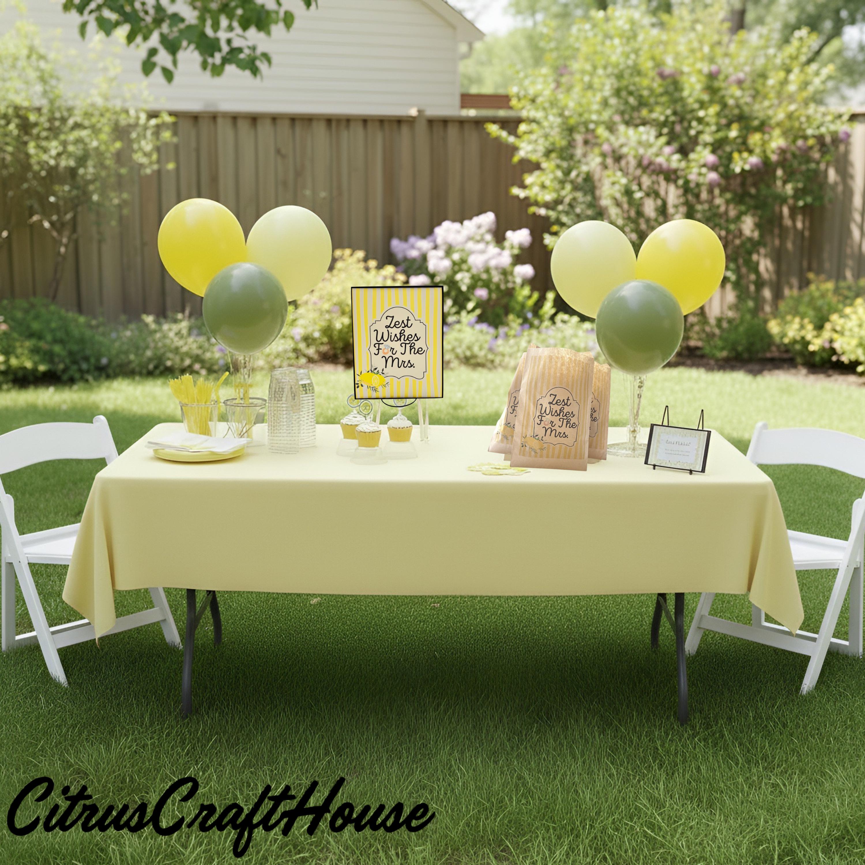 A yellow tablecloth-covered party table set up outdoors on a grassy lawn, decorated with yellow and green balloons, white folding chairs, paper bags, and a sign that reads 'zest wishes For The Mrs.' A CitrusCraftHouse watermark appears at the bottom left.
