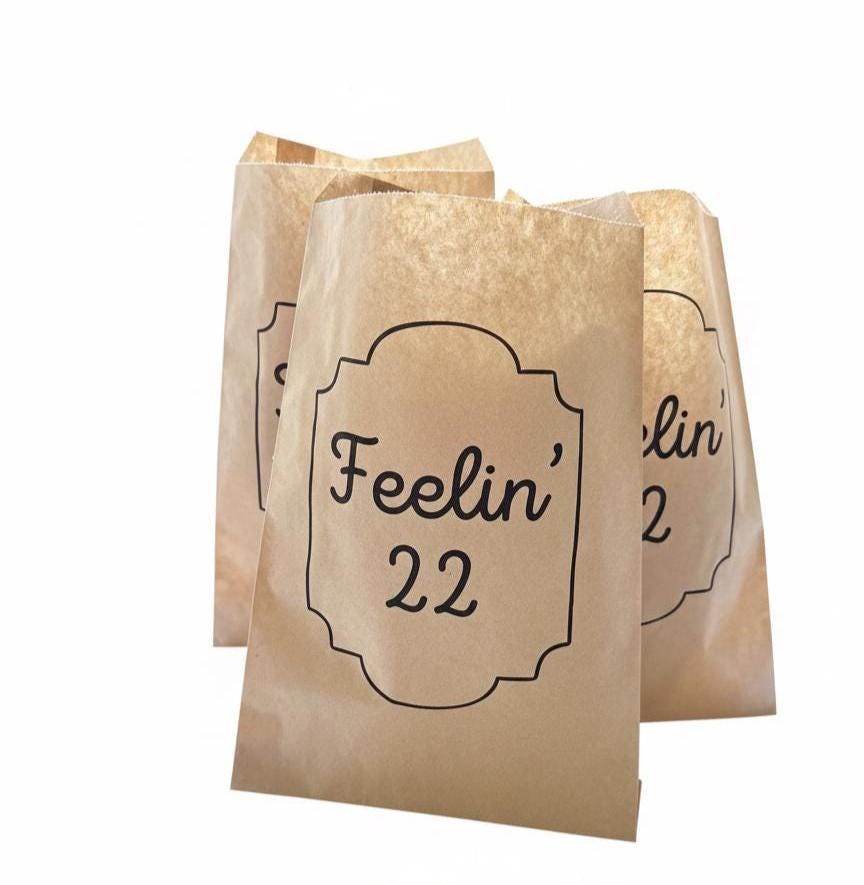 Three small kraft paper party favor bags with black printed text reading 'Feelin' 22' on a plain white background.
