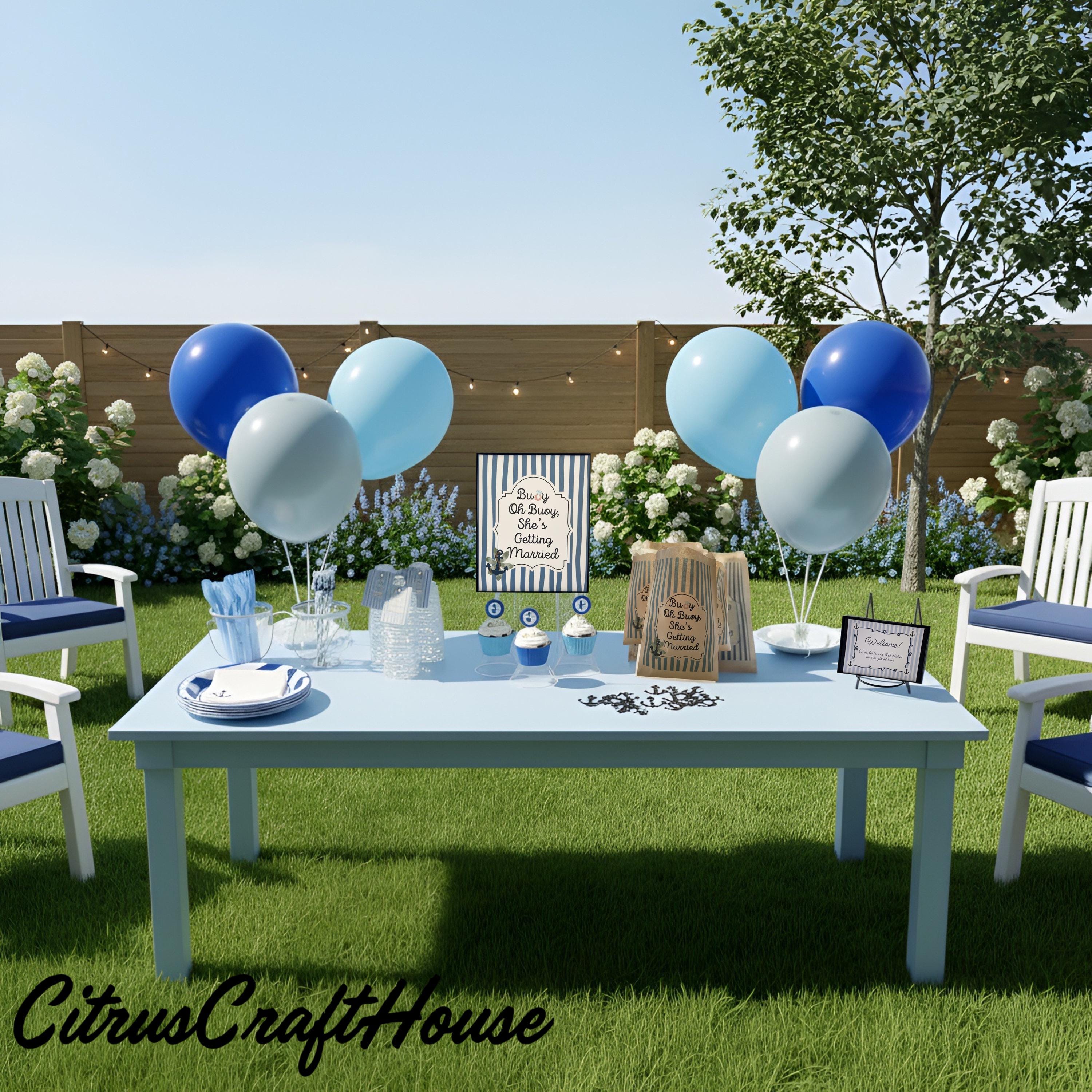 Outdoor birthday party setup on a lawn with a light blue table, blue and white balloons, white chairs, and a sign that  Reads   Buoy oh buoy she’s getting marriedCitrusCraftHouse.