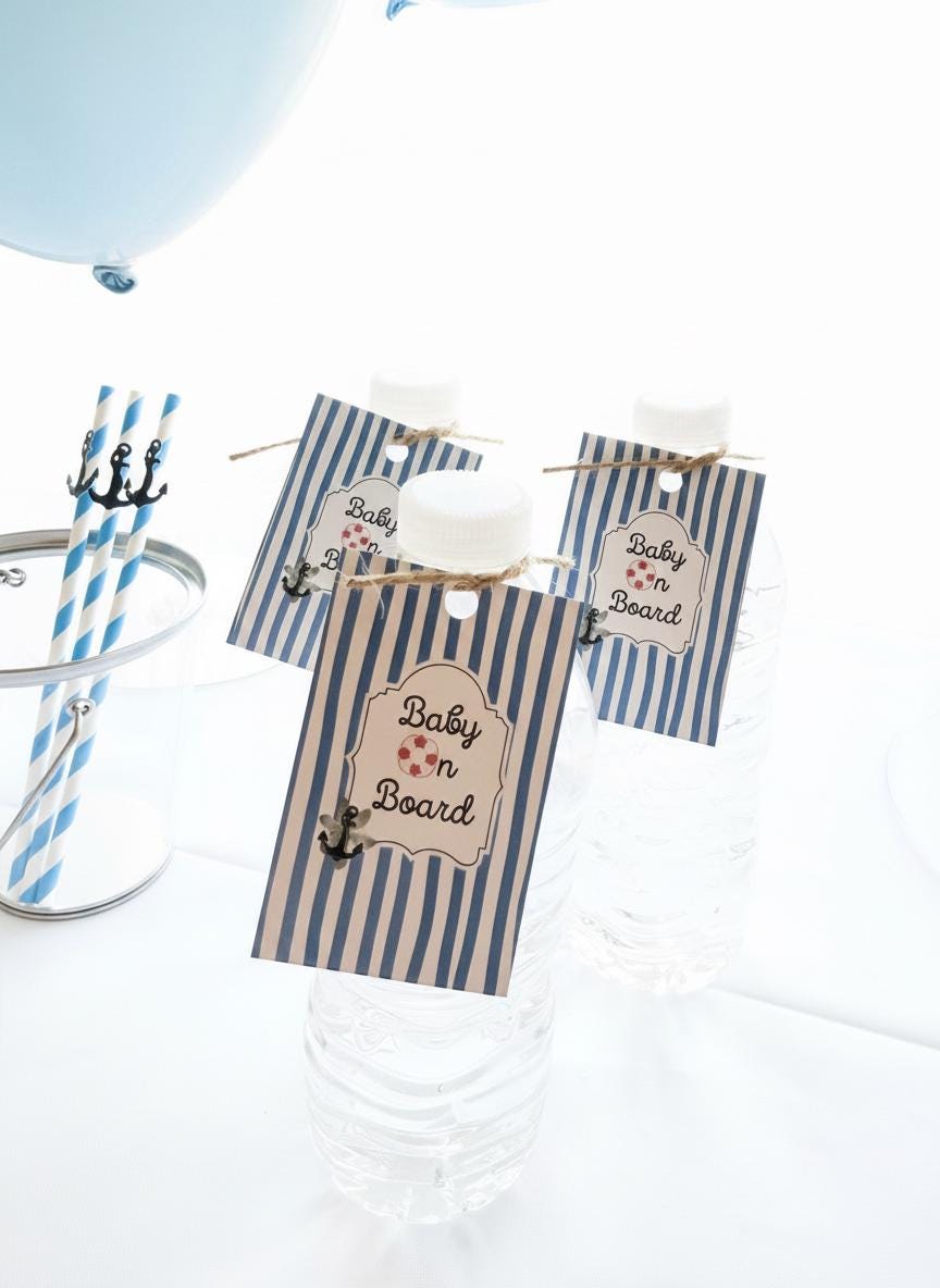 Three clear plastic water bottles with white caps, each decorated with a navy and white striped paper tag that says 'Baby on Board' with a small anchor graphic. Blue-and-white striped straws in a glass and part of a blue balloon are visible in the bright white setting.