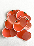 A pile of die-cut stickers shaped like sliced oranges, featuring a glossy orange-red surface with a white border, set against a textured off-white background.