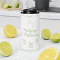 A white insulated can cooler sleeve with green line art and the text 'Mahjong & Matrimony' stands on a white countertop, surrounded by lemon slices and limes, with a blurred kitchen background.