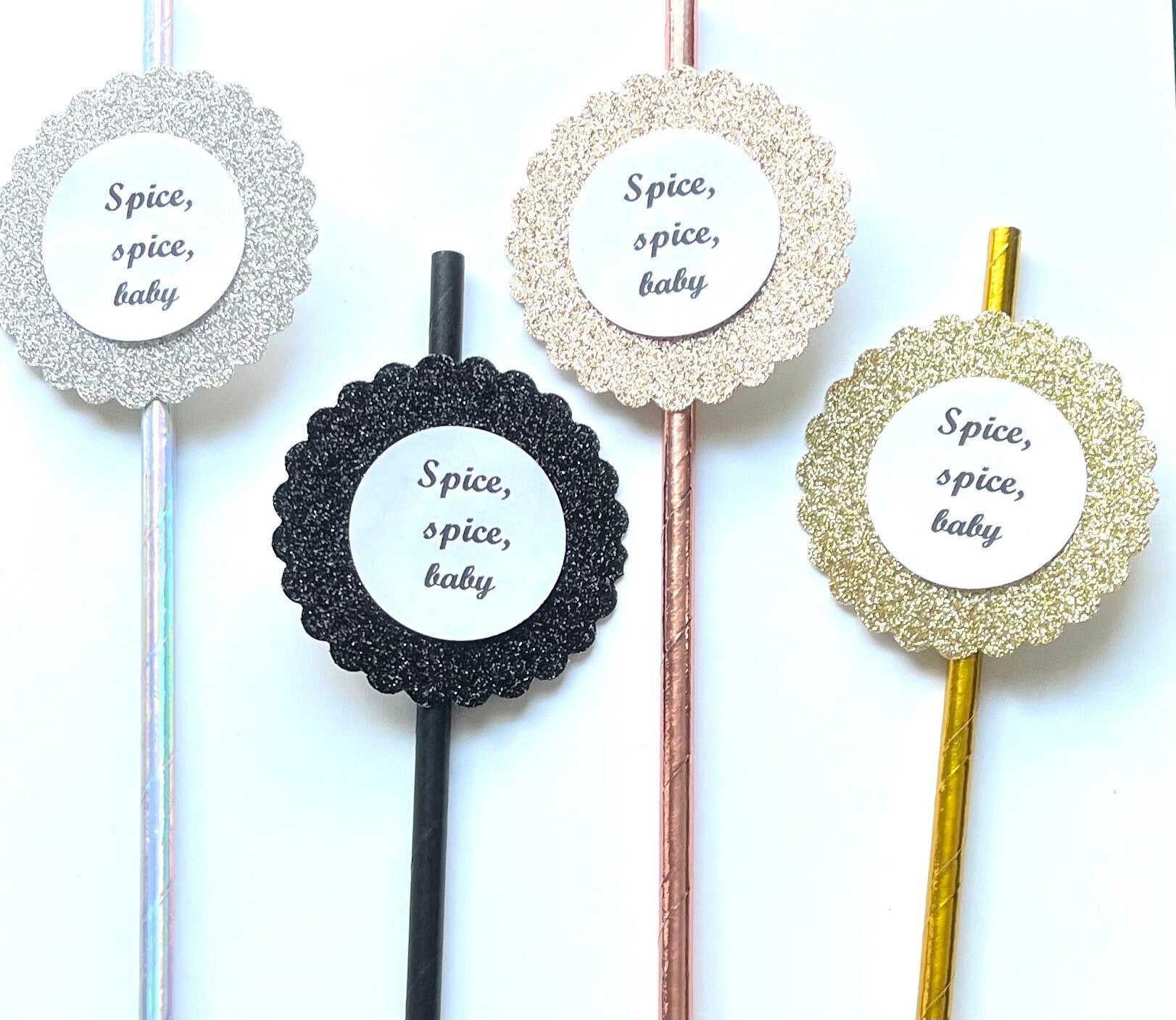 Four decorative straws with round glittery scalloped end pieces and white center labels reading 'Spice, spice, baby' on a white background.