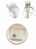 A set of disposable party tableware on a white background, including a white paper plate with a folded cream napkin printed with a small coffee cup and heart, a clear wire bucket filled with white plastic utensils, and a clear cup holding wooden chopsticks with a heart-shaped holder.