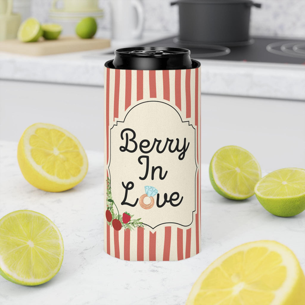 A slim can cooler sleeve with red and white vertical stripes and a cream label reading 'Berry In Love' with berry illustrations, shown around a black can on a kitchen countertop with lemons and limes around it.