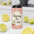 A slim can cooler sleeve with red and white vertical stripes and a cream label reading 'Berry In Love' with berry illustrations, shown around a black can on a kitchen countertop with lemons and limes around it.
