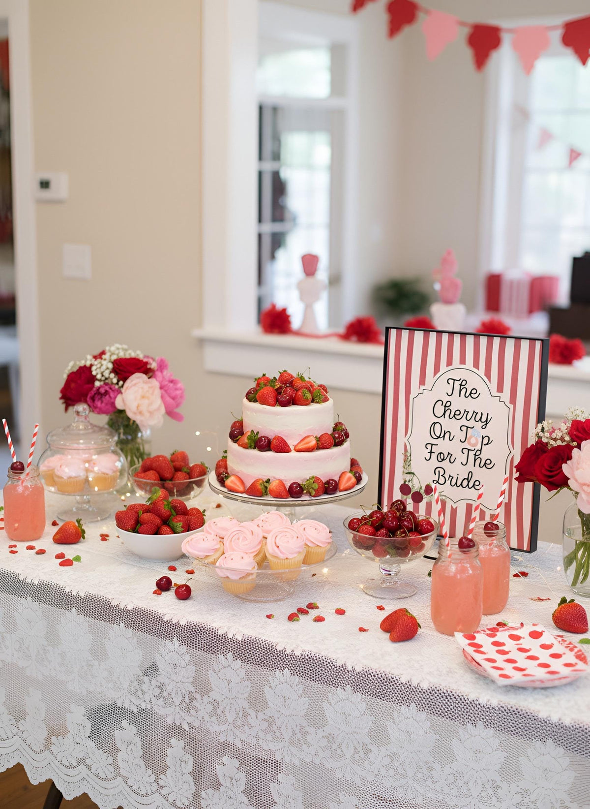A Valentine's Day themed bridal shower dessert table decorated with strawberries, pink cupcakes, glasses of pink drink, and a sign that reads 'The Cherry On Top For The Bride'.