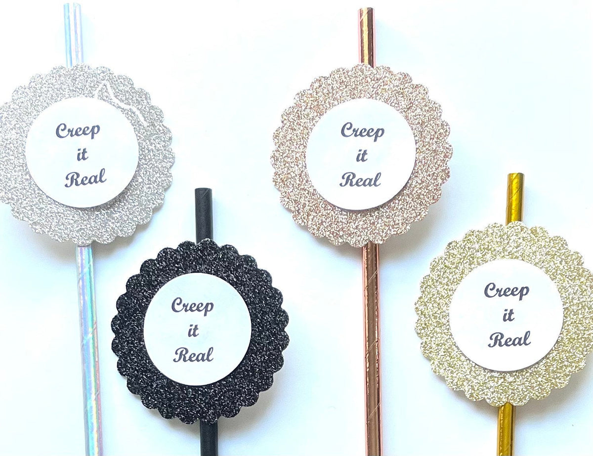 Four decorative round paper straws with the phrase 'Creep it Real' printed in gray script on white centers, arranged on metallic sticks against a plain white background. The stickers feature silver glitter, black glitter, champagne glitter, and gold glitter designs.