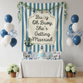 A nautical-themed baby shower party setup featuring a large blue and white striped backdrop banner with the text 'Buoy Oh Buoy, She's Getting Married' and an anchor design. The setup includes a decorated table with a white tablecloth, a blue and white tiered cake, photo frames, and blue, white, and navy balloons on both sides.